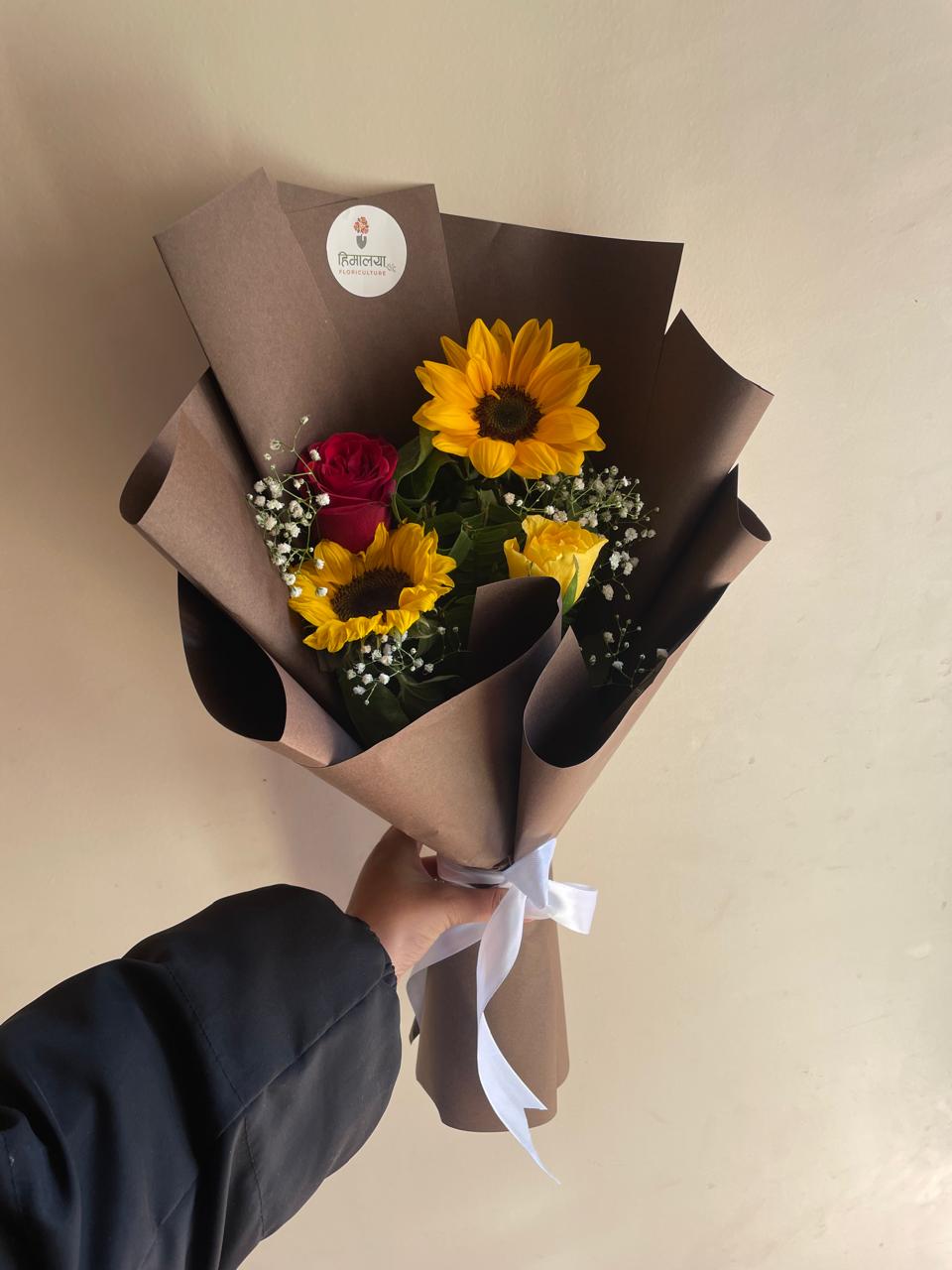 The ultimate mood-booster! A delightful arrangement featuring 2 radiant single-stem sunflowers, 1 elegant red rose, and 1 cheerful yellow rose, all nestled among fresh seasonal fillers.