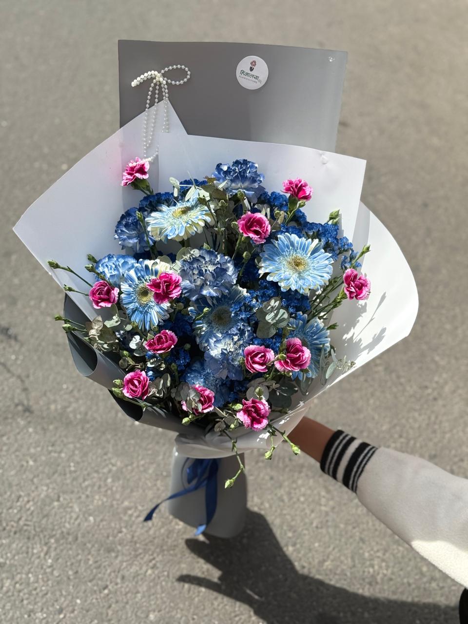 As flowers are natural products, the size, bloom stage, and shades of flowers may vary slightly depending on seasonal availability. Spray carnation fillers may be replaced with gypsy flowers based on availability during the season while maintaining the bouquet's overall design and premium appearance. The wrapping style may also vary slightly while ensuring an elegant presentation. To keep the flowers fresh for longer, place them in clean water and keep the bouquet away from direct sunlight and excessive heat.